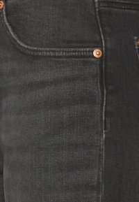 Jeans de denim negro que presentan una textura suave, detalles en herrajes de cobre y un diseño clásico de cinco bolsillos con sutiles detalles de costura.