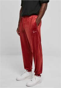 Red velvet jogger pants with elastic waistband and cuffs, side pockets, and embroidered logo accent; paired with white sneakers.