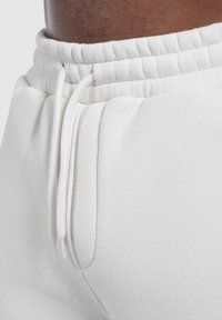 Weiße Jogginghose aus strukturiertem Stoff, mit elastischem Bund und Kordelzug sowie seitlichen Taschen für Funktionalität.