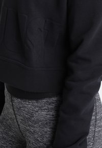 Felpa nera cropped con la scritta "JUST" in rilievo sul davanti, dotata di maniche lunghe e una texture liscia, abbinata a leggins grigi con texture.