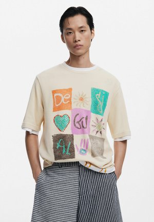 Short-sleeve cream T-shirt featuring a patchwork design with various colored graphics, including hearts, sun, and handprints; textured fabric.