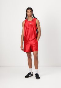 Red athletic tank top and shorts made of shiny fabric, featuring black accents and the Adidas logo. Worn with black shoes and white socks.