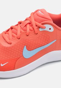 Baskets en maille corail avec un logo Swoosh bleu clair, des accents blancs contrastants, une tige texturée et une semelle blanche plate. Les lacets sont également corail.