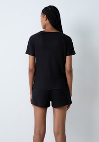Completo loungewear nero composto da una maglietta a maniche corte e pantaloni corti, realizzato in un tessuto morbido e leggero con una vestibilità comoda e una texture sottile.