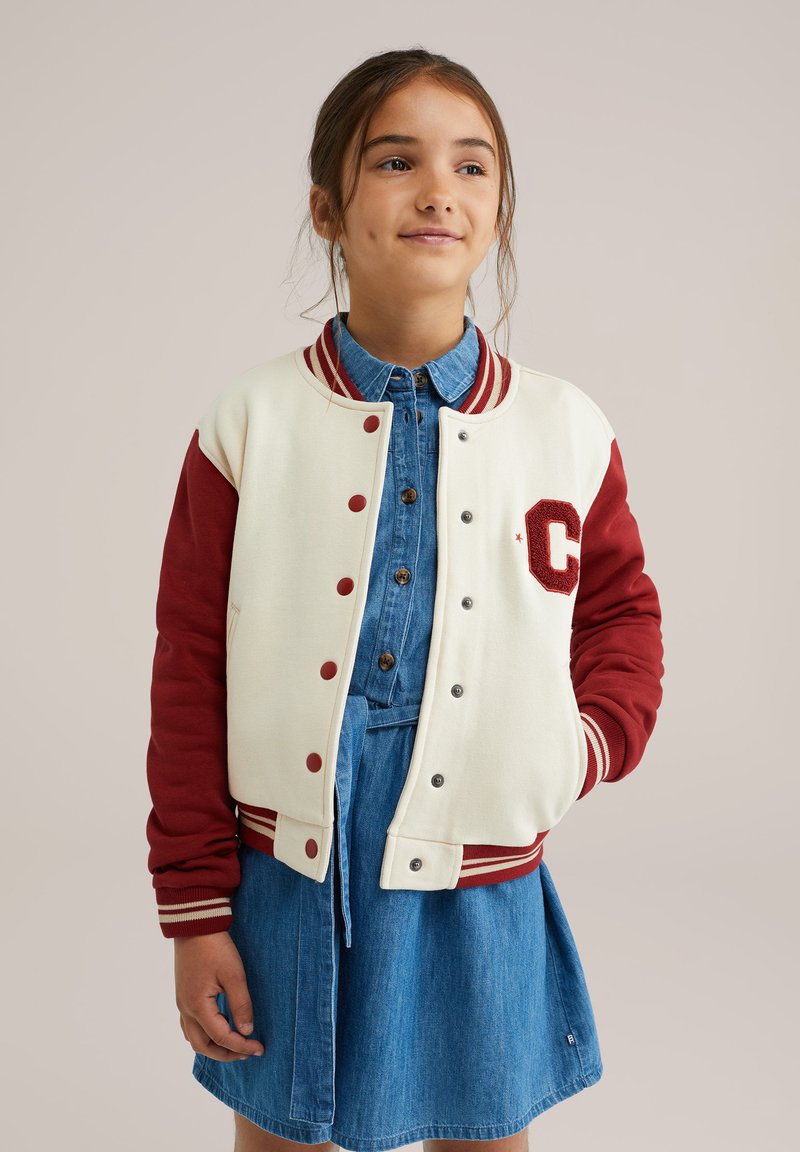 Vit och vinröd varsityjacka med randig ribbad krage, knappstängning och en bokstav "C"-applikation, bärs över en denimklänning.