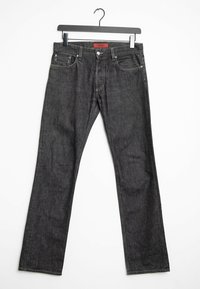 Jeans in denim grigio scuro con design a gamba dritta, cinque tasche e cuciture a contrasto, appesi a un gancio in metallo nero.