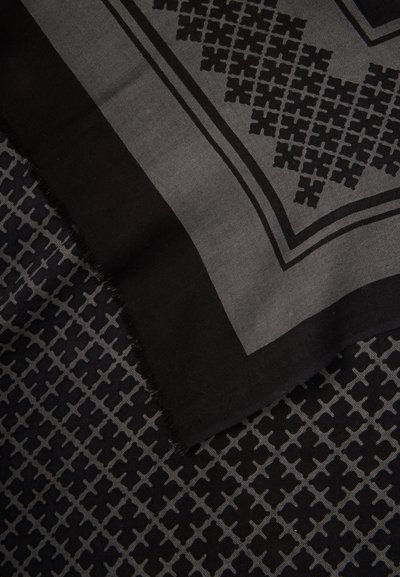 Tissu noir et gris avec un motif géométrique en croix, présentant un coin plié montrant une texture en couches et des bords effilochés.