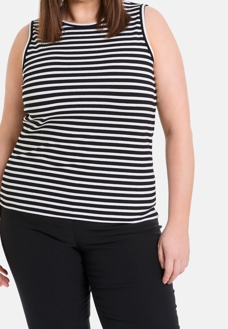 Černobílé pruhované bezramínkové tričko s ribbovou texturou, spárované s černými kalhotami. Tričko má kulatý výstřih a přiléhavý střih.