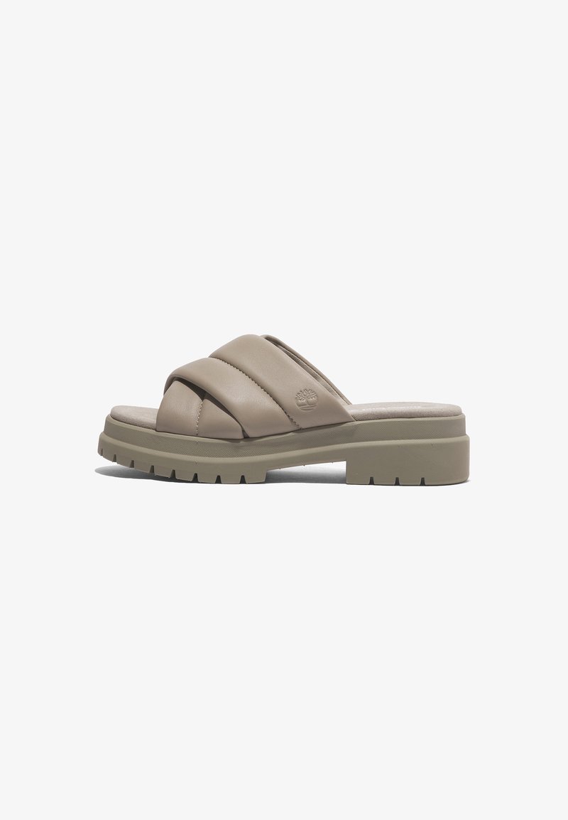 Sandale beige à enfiler avec des brides épaisses et rembourrées en croix et une semelle épaisse rainurée, avec un petit logo arbre embossé sur le côté.