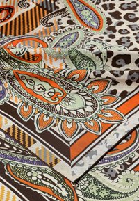 Multicolored patterned fabric featuring paisley, floral, and geometric designs in orange, green, blue, and black on a cream background.