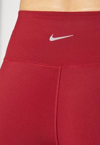 Rdeče atletske legice, izdelane iz raztegljive tkanine. Imajo visok pas in siv logotip Nike Swoosh. Opazen šivni detajl na šivih.