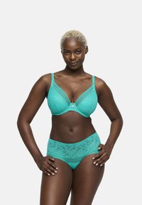 Reggiseno in pizzo color turchese con scollatura profonda e dettagli stampati, abbinato a una mutandina alta coordinata, entrambe con una texture liscia.