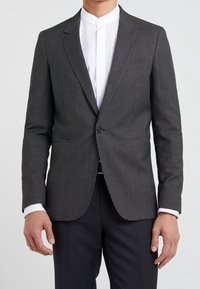 Czarny i biały blazer w wzory o dopasowanym kroju, z zapięciem na jeden guzik i klapami, w połączeniu z białą koszulą bez kołnierzyka.