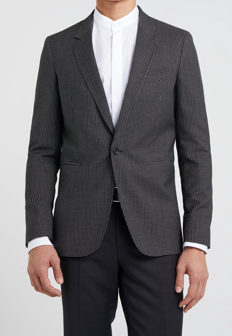 Czarny i biały blazer w wzory o dopasowanym kroju, z zapięciem na jeden guzik i klapami, w połączeniu z białą koszulą bez kołnierzyka.
