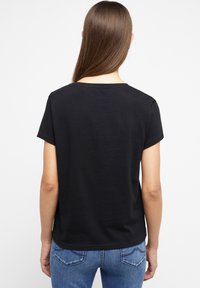 Černé bavlněné tričko s krátkými rukávy, klasickým výstřihem a volným střihem. Hladká textura s jednoduchým designem, nošeno s modrými džíny.