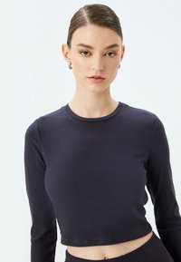 Langærmet, crew-neck crop top i mørk marineblå ribbet stof, der har en struktureret overflade og en tætsiddende pasform. Synlig mave ved kantlinjen.