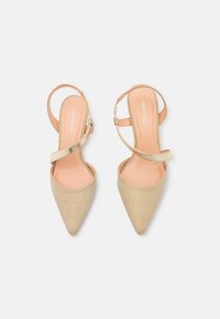 Escarpins slingback à bout pointu en tissu métallisé doré avec une finition texturée. Présente une fine bride à la cheville et une semelle intérieure nude unie.