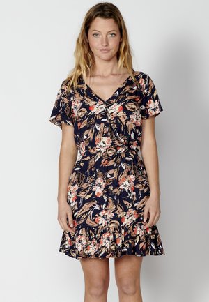 Vestido floral en azul marino con patrones en rosa, naranja y crema. Presenta mangas cortas, un escote en forma de V, cintura fruncida y un dobladillo con volantes.
