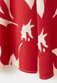 Tissu rouge et blanc avec un grand motif floral abstrait et une texture visible, bord ourlé en bas.