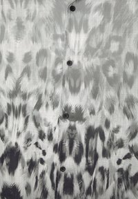 Tissu à motifs gris et noir avec un design d'imprimé animal flou et des boutons noirs visibles le long de la couture centrale.