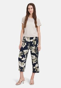 Jasnobeżowy teksturowany top z krótkim rękawem z półprzezroczystymi akcentami zestawiony z granatowymi, kwiatowymi spodniami o długości 7/8, ozdobionymi zielonymi i białymi kwiatowymi wzorami.