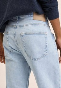 Jeans de mezclilla azul claro con un diseño ajustado, bolsillos traseros con costuras en forma de V y una etiqueta de cuero color marrón en la pretina.