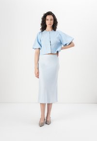 Lys blå, cropped, teksturert bluse med puffede ermer, parret med en matchende, glatt, midilengde skjørt og beige spisse hæler.