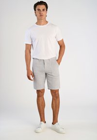 Vit bomull t-shirt tillsammans med ljusgrå randiga shorts. Shortsen har en rak front och sidofickor, accentuerade av vita sneakers.