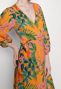 Sukienka w kwiaty w kolorze pomarańczowym, z różowymi i zielonymi tropikalnymi wzorami, długimi puff sleeves i wiązanym detalem w talii. Miękka tekstura tkaniny.