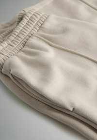 Helle beige Sweatpants aus weichem Material mit elastischem Bund und Seitentaschen, die subtile Nähte aufweisen.