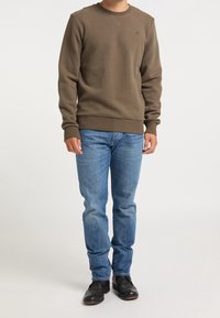 Brown crewneck sweatshirt with ribbed cuffs and hem, paired with light blue jeans and black footwear, standing against a neutral background.