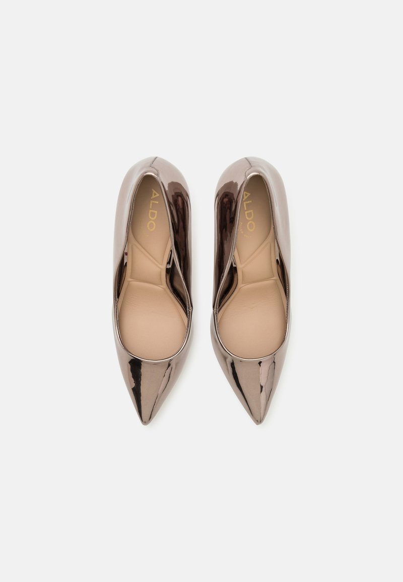 Des chaussures à talons hauts et à bout pointu en vernis taupe foncé brillant, avec une semelle intérieure beige douce et des détails de marque à l'intérieur.