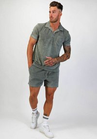 Kortärmad skjorta med krage och matchande shorts i mjukt grönt tyg. Har en bröstficka, dragsko i midjan och vita sneakers.