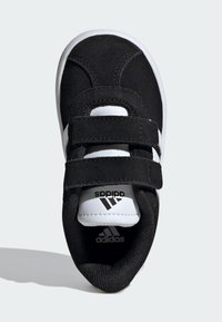 Černé semišové tenisky s dvěma suchými zipy, bílými akcenty a gumovou podrážkou. Logo Adidas je umístěno na jazyku a straně.