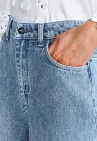 Jeans in denim azzurro chiaro con vita alta, dotati di chiusura a bottone, tasche anteriori e una texture leggermente sbiadita.