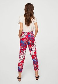 Pantalons floraux avec une base rouge ornée de fleurs bleues et blanches, taille haute, coupe droite et texture de tissu douce.