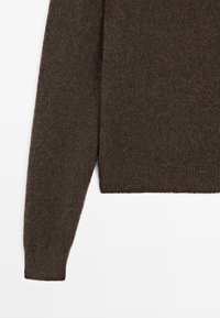 Pull en tricot marron à manches longues, avec un motif texturé et un ourlet côtelé. Tissu doux et chaud avec une apparence légèrement épaisse.