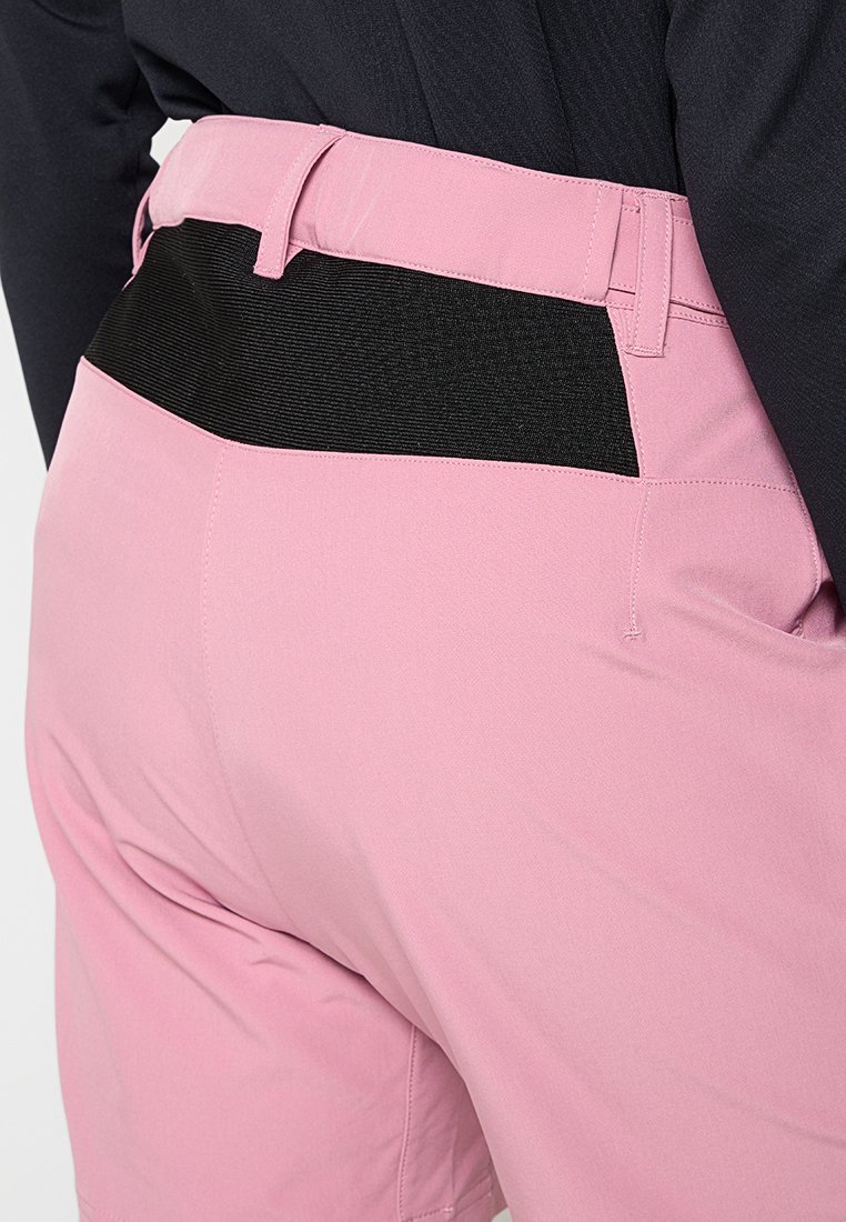 Rückansicht einer Person, die rosa Hosen mit einem breiten schwarzen elastischen Bund und einem schwarzen Shirt, das eingesteckt ist, trägt.