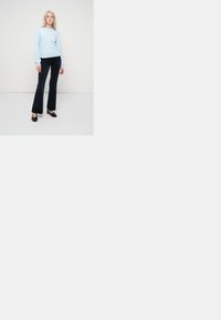 Gaiši zils garais piedurkņu tops apvienots ar melniem izplešamajiem biksēm. Audums izskatās mīksts, un piegriezums ir brīvs. Melnas kurpes noslēdz komplektu.