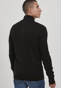 Pull en maille noire avec un col montant, des poignets et un ourlet côtelés, et une texture douce. Conçu pour une silhouette ajustée.