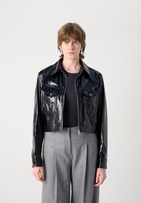 Felsőrészen elvágott fekete patent bőr dzseki, két mellzsebbel és cipzáros zárással, szürke bő szabású nadrággal és fekete, testhezálló toppal párosítva.