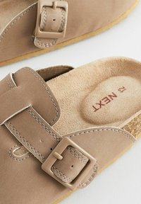 Beige suede sandaler med justerbar rem, der har en plastikspænde, glat inderside og polstret fodseng. Let syninger som accent.