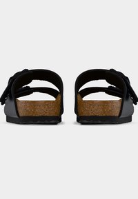 Ζευγάρι μαύρα σανδάλια ανοιχτής μύτης με πέλματα φελλού και ρυθμιζόμενους ιμάντες, φανερά από πίσω με φόντο απλό λευκό.