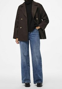 Mörkbrun dubbelknäppt kappa med guldknappar, svart polotröja och vida blå denimjeans. Svarta platåskor fulländar outfiten.