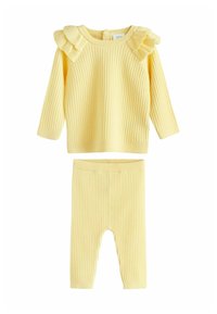 Costum din două piese din tricot ribat galben, compus dintr-o bluză cu mânecă lungă și accente din volane pe umeri și o pereche de colanți asortați cu un chivă elastică.