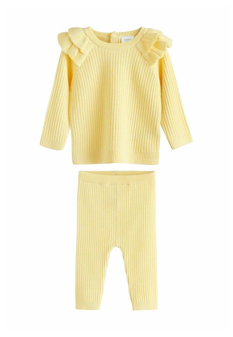Costum din două piese din tricot ribat galben, compus dintr-o bluză cu mânecă lungă și accente din volane pe umeri și o pereche de colanți asortați cu un chivă elastică.