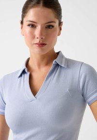 Polo bleu clair avec une texture côtelée, col en V, manches courtes et un logo sur la poitrine. Doté d'un col contrastant.