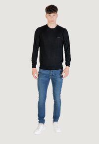 Maglione nero a maniche lunghe con scollatura rotonda, abbinato a jeans azzurri e scarpe da ginnastica bianche. Design semplice con una leggera texture.
