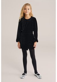 Melnas samta kleita ar baltām punktiņām, garām piedurknēm un sašaurinātu vidukli. Saskaņota ar melnām zeķbiksēm un sudraba balerīnu apaviem.