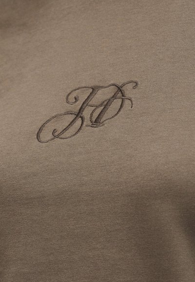 Σκούρα καφέ κεντημένα διαπλεκόμενα γράμματα «H» και «O» σε φόντο από ανοιχτό καφέ ύφασμα.